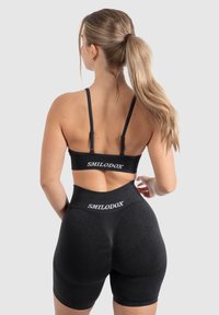 Zwarte sportset met een cropped top met verstelbare bandjes en high-waisted shorts. Beide items hebben "SMILODOX" logo-details.