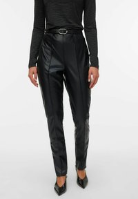 Melni mākslīgo ādas bikses ar augstu jostasvietu, piedāvā vertikālas šuves un jostu. Bikses ir piegrieztas un cieši pieguļošas, ar gludu tekstūru.