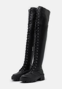 Czarne skórzane buty do kolan z przednim sznurowaniem, srebrnymi oczkami i bocznym zamkiem. Gruba, fakturowana podeszwa zapewniająca dodatkową przyczepność i trwałość.