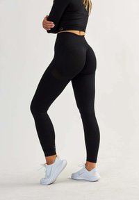 Leggings neri realizzati in tessuto elastico, con vita alta e design aderente. Abbinati a scarpe da uomo bianche.
