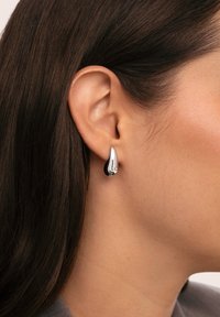 Pendientes en forma de lágrima de plata con un acabado pulido, que presentan una superficie lisa y un sutil detalle cerca de la parte superior.