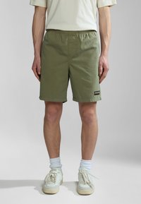 Green cotton shorts with an elastic waistband, featuring a small logo patch, and a relaxed fit. Paired with white sneakers and light blue socks.