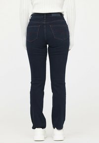 Vaqueros de mezclilla azul oscuro con un estilo ajustado, que presentan dos bolsillos traseros con costuras rojas en contraste y una textura suave.