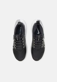Black athletic shoes with a textured upper, gray laces, and a white sole. Features a breathable mesh design and Nike branding inside.