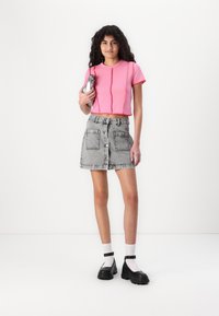 Ροζ κοντομάνικη μπλούζα με υφή, συνδυασμένη με γκρι τζιν φούστα με μπροστινά κουμπιά και μεγάλες τσέπες. Φοράνε μαύρες πλατφόρμες.