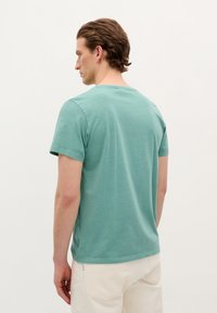 Mint green cotton t-shirt with short sleeves, round neckline, and a relaxed fit, featuring a side seam accent near the hem.