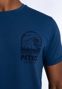 Marineblauwe katoenen t-shirt met een grafische print van golven en de tekst "PETROL WAVERIDERS" in het zwart op de linker borst.