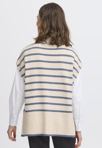 Beżowy sweter bez rękawów z niebieskimi paskami, z prążkowanym dołem i bocznymi rozcięciami. Nosi się go na białej koszuli z guzikami.