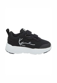 Chaussure de sport noire avec tige en mesh, semelle en caoutchouc blanche et sangles en velcro. Présente un graphique signature en blanc sur le côté.