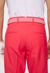 Roze katoenen broek met een gevlochten roze riem, voorzien van twee achterzakken met knopen en een gladde textuur.