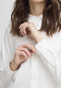 Camicia bianca a maniche lunghe con colletto classico, dotata di polsini a doppio bottone. Tessuto morbido e leggero con un aspetto nitido.