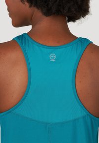 Bakifrån av en person med mörk hud som bär en ärmlös atletisk tröja i teal med "ATG Wrangler"-logotypen nedanför halsringningen.