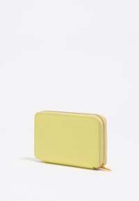Cartera de cuero amarilla con superficie texturizada, forma rectangular, cremallera dorada y diseño minimalista. Mide aproximadamente un tamaño mediano.