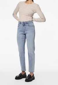 Top de manga larga a rayas en beige y blanco, jeans de tiro alto en azul claro y mocasines negros con plataforma. Diseño simple, ajuste casual.