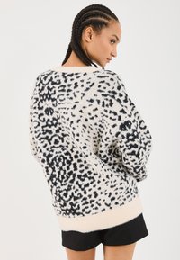 Oversized sweater in white with a black animal print. Soft, textured fabric with dropped shoulders and a wide, contrasting hem.
