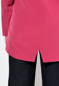 Rosa långärmad tunika med böjd nederkant och sidoklipp. Tyget har en slät yta. Kombineras med mörkblå denimbyxor.