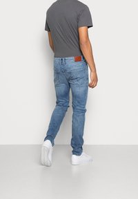 En grå passformst-shirt för män som är kombinerad med ljusblå denimjeans. Jeans har en brun läderlapp på baksidan av midjan och är ankellånga.