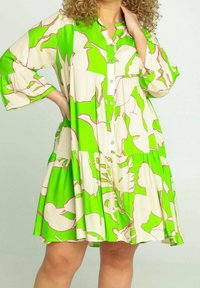 Groene en crèmekleurige, gelaagde jurk met botanische print. Voorzien van knoopsluiting, driekwartmouwen en zachte stoftextuur.