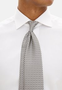 Gray patterned tie with circular designs in darker gray and white against a light background; worn with a white dress shirt.