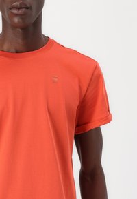 Oransje bomull t-skjorte med rullede ermer, med en liten hevet logo på brystet. Glatt tekstur og vanlig passform.
