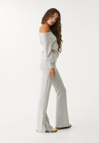 Světle šedý, top bez ramínek, spárovaný s odpovídajícími kalhotami s rozšířenými nohavicemi a bočními rozparky. Materiál je měkký a hladký.