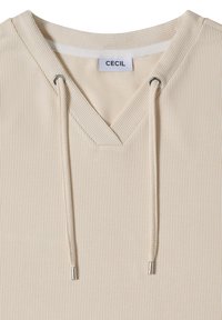 Haut à capuche en tissu côtelé beige avec col en V et cordons dotés d'embouts métalliques, avec une étiquette de marque "CECIL" à l'intérieur du col.