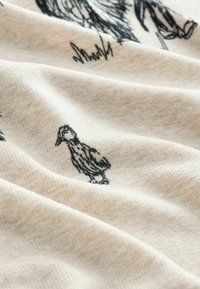 Lysebeige stof med en blød tekstur, prydet med sorte illustrationer af fugle, herunder en and, på en let krøllet overflade.