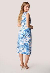 Ärmelloses Kleid aus weißem Stoff mit blauem tropischem Blätterdruck, knielang, mit taillierter Silhouette und seitlichem Schlitz.