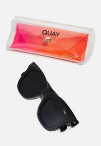 Black rectangular sunglasses with dark lenses and a bold frame, displayed alongside a clear orange gradient case with the word "QUAY."