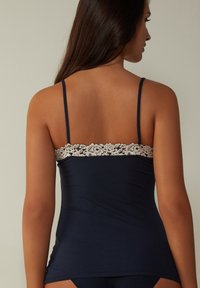 Débardeur bleu marine avec des bretelles fines, orné d'une bordure en dentelle florale blanche le long du dos. Tissu doux et extensible, design ajusté.