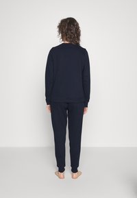 Completo sportivo di colore blu scuro composto da una maglia a maniche lunghe e pantaloni tapered. Tessuto morbido con polsini a costine e vestibilità comoda.