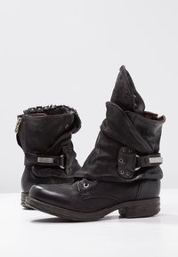 Botines negros de cuero con un diseño holgado, detalles de herrajes plateados y una parte superior en capas. Presentan una puntera redonda y cierre lateral con cremallera.