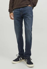 Pantalones vaqueros de mezclilla azul oscuro con un diseño de pierna recta, sutil desgaste en la tela y un estilo clásico de cinco bolsillos, combinados con zapatillas negras.