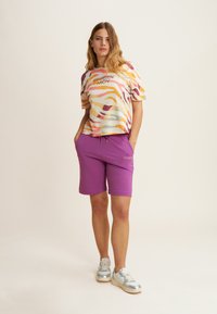 T-shirt con motivo astratto multicolore; maniche corte. Pantaloni corti viola con cordoncino e tasche. Sneakers argentate con finiture lucide.