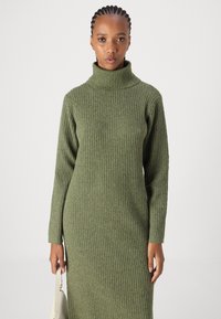 Πράσινο ριγωτό πλεκτό φόρεμα με ψηλό λαιμό, μακριά μανίκια και πλάγια σχισμή. Το υλικό έχει απαλή υφή και εφαρμοστή σιλουέτα.