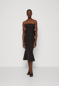 Schwarzes trägerloses Kleid mit tailliertem Oberteil und weit ausgestelltem Saum. Hergestellt aus glattem Stoff, mit seitlichen Ausschnitten und minimalen Details.