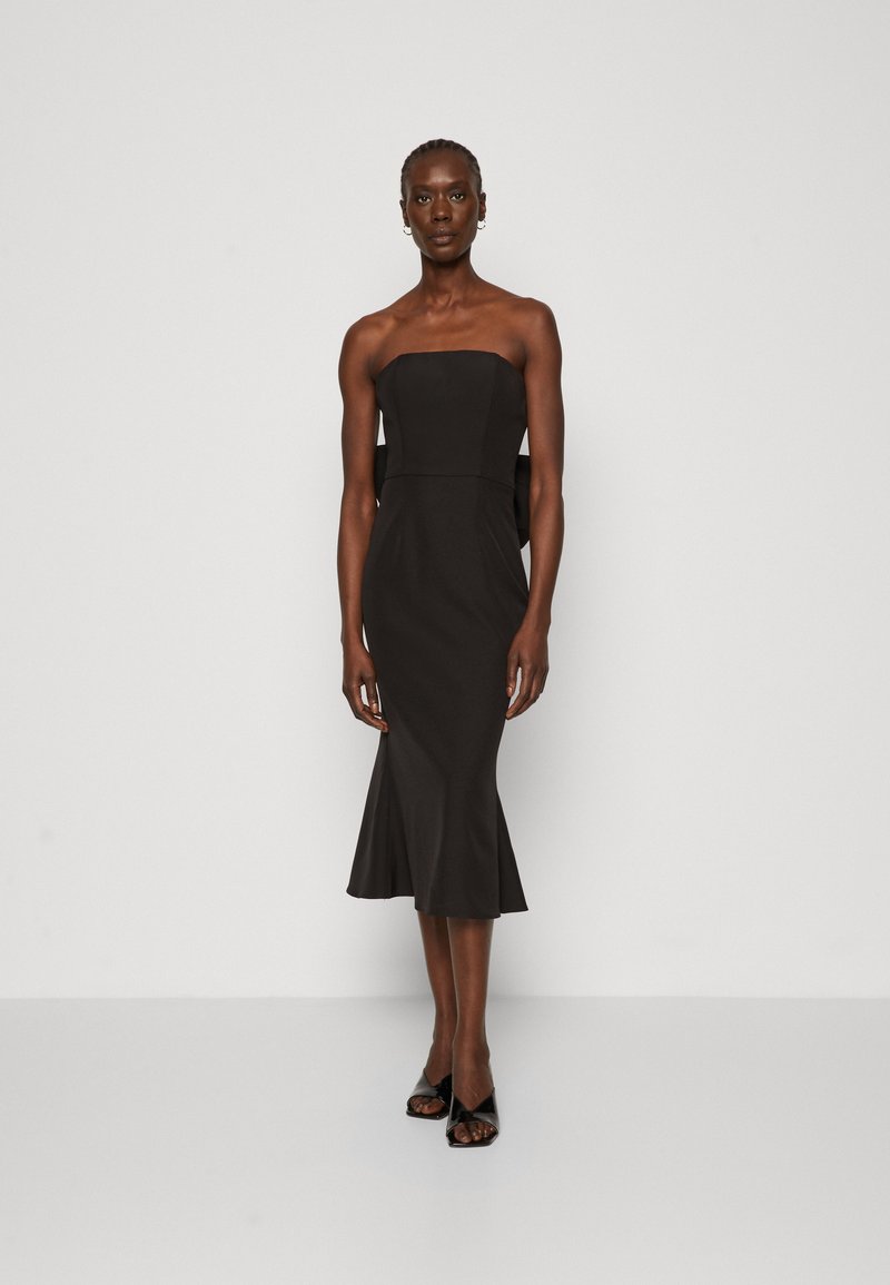 Robe noire sans bretelles avec un corsage ajusté et un ourlet évasé. Fabriquée en tissu lisse, elle présente des découpes latérales et un minimum de détails.