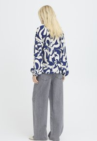 Locker sitzende, gemusterte Bluse in Marineblau und Creme, lange Ärmel, kombiniert mit hoch taillierten, weit geschnittenen grauen Jeans. Glatte Stoffstruktur.