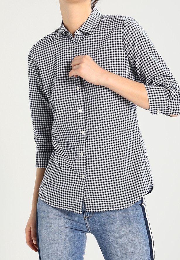 Personne portant une chemise à carreaux noir et blanc boutonnée avec des manches trois-quarts et un jean bleu avec une bande latérale foncée.