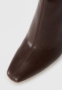Bottine en cuir marron avec un bout pointu, dotée d'une couture verticale et d'une texture lisse. Le talon n'est pas visible sur l'image.