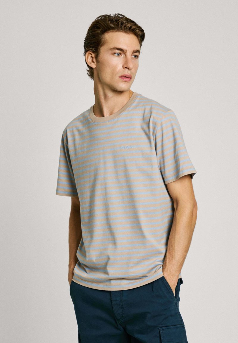 Juostuota šviesiai ruda ir mėlyna marškinėliai, pagaminti iš minkštos medvilnės. Turi apvalų kaklą, trumpas rankoves ir subtilų prekės ženklą ant krūtinės.