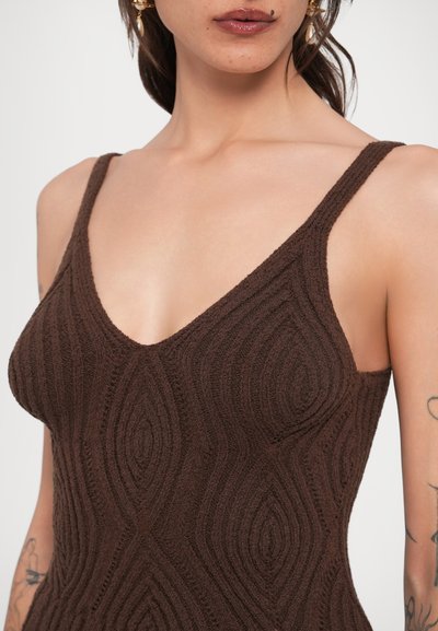 Καφέ πλεκτό φόρεμα με V-λαιμόκοψη, λεπτές τιράντες και υφασμάτινο μοτίβο με κυματιστά σχέδια. Κοντινή όψη των λεπτομερειών του υφάσματος.