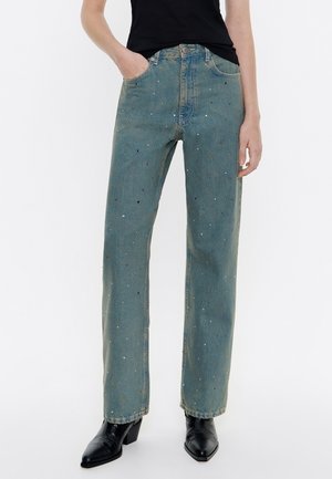 Jeans in denim blu chiaro con vestibilità dritta, decorati con piccole paillettes multicolori, abbinati a stivaletti neri con tacco.