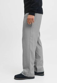 Pantaloni gri cu o croială dreaptă, realizati dintr-un material texturat, cu buzunare laterale și un front plat. Purtați cu un pulover negru și pantofi închiși la culoare.