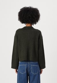 Olive green cropped sweater with a ribbed texture, wide sleeves, and a round neckline, paired with high-waisted blue denim jeans.
