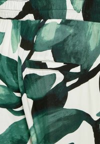 Vitt tyg med stora gröna och svarta lövmönster, med ett elastiskt midjeband och en liten rektangulär ficka.