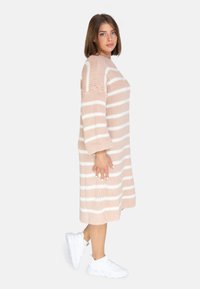 Strickkleid in Hellrosa mit weißen horizontalen Streifen, mit einem lockeren Schnitt, langen Ärmeln und einem gerippten Kragen. Tragen mit weißen Sneakers.