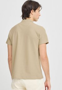 Polo shirt beige a maniche corte con orlo dritto e scollatura tonda, realizzato in tessuto liscio, mostrato di spalle.