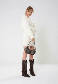 Krämfärgad stickad klänning med figurnära siluett. Bruna mocka cowboystövlar med broderade detaljer. Mörkgrå läderväska med silverdetaljer.