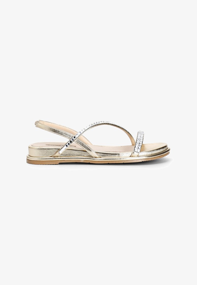 Sandalias metálicas doradas con suela plana, correas entrelazadas y adornos de strass a lo largo de la correa superior para un detalle adicional.